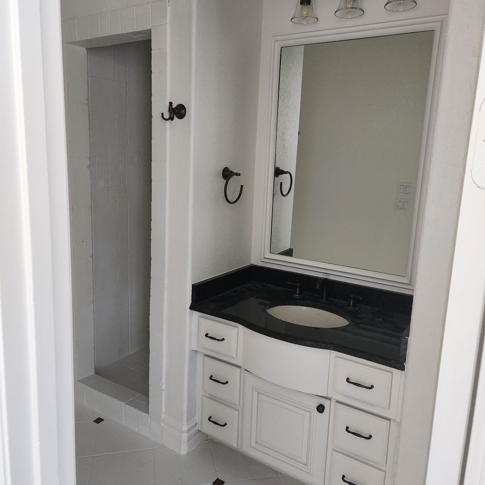 White bathroom with black countertop, mirror, and a shower.
