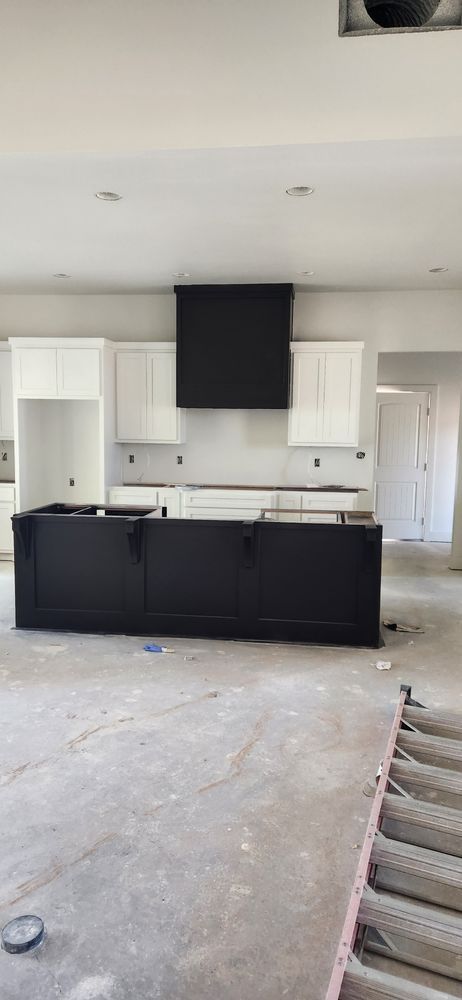 Newly built kitchen with black island, white cabinets, and black hood. Concrete floor.