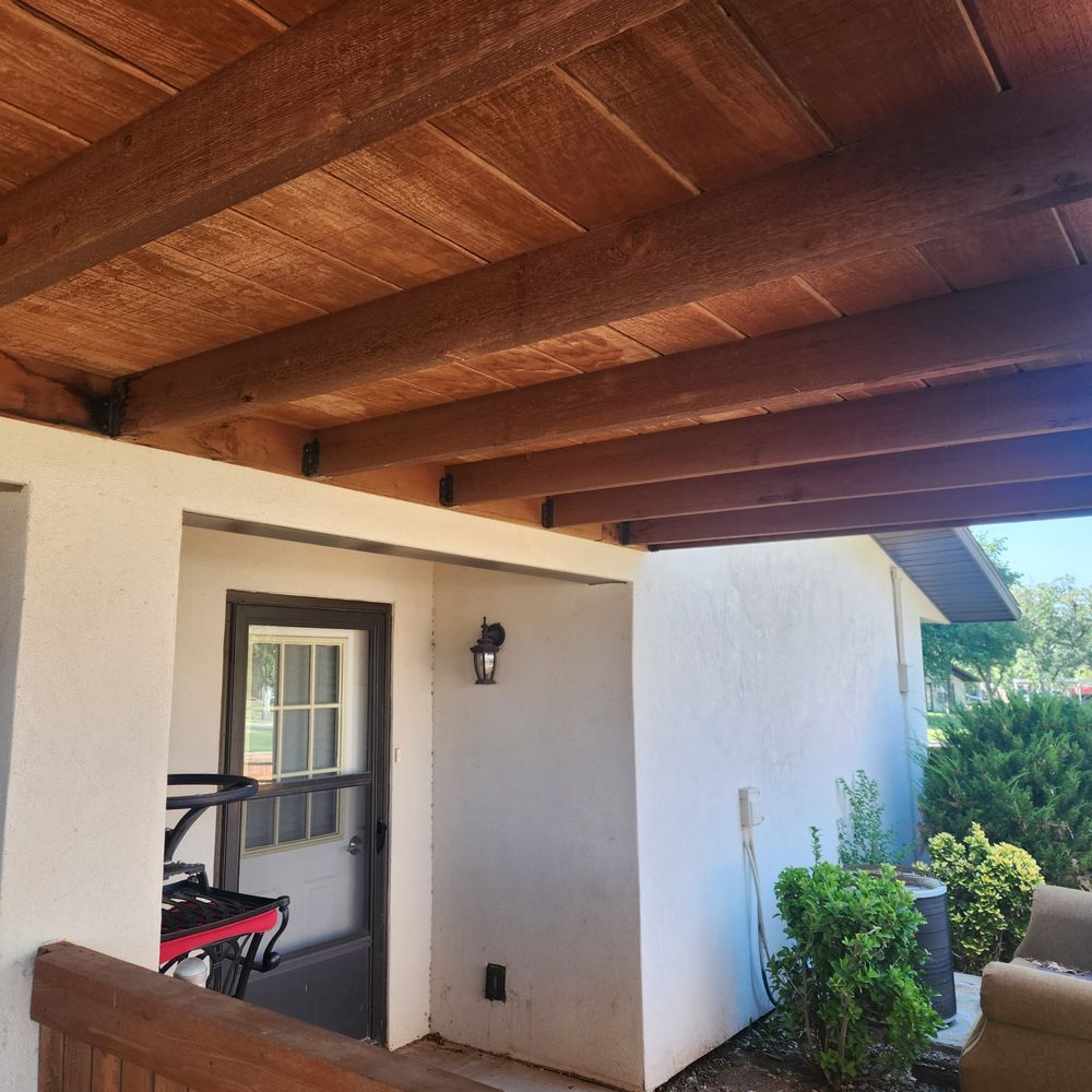 Wooden beam ceiling over an outdoor area with a door, white stucco walls, and plants.