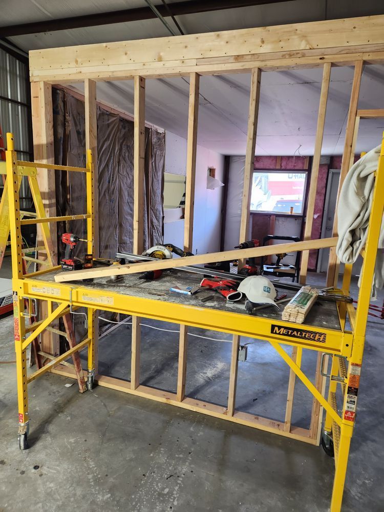 Yellow scaffolding supports tools near a partially built wooden wall inside a building.