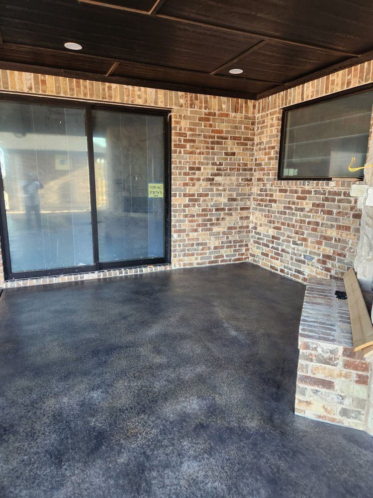 Brick-walled outdoor space with a dark, textured floor. Large sliding glass door and small window present.