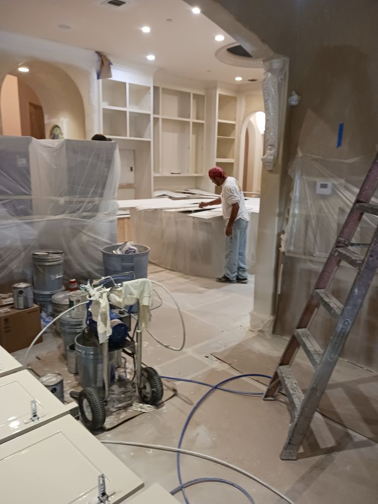 A person painting a kitchen with a sprayer. Cabinets and island are covered.