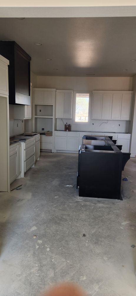 A partially completed kitchen. White cabinets, black island, concrete floor.