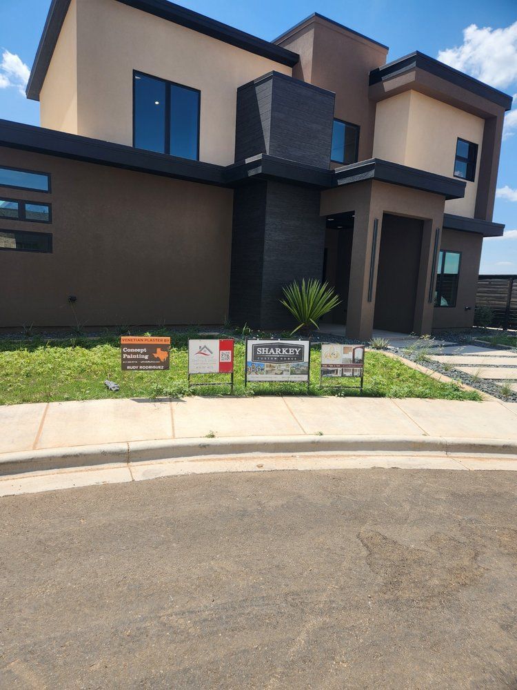 Modern two-story house with real estate signs on the lawn. Brown and black exterior, blue sky.