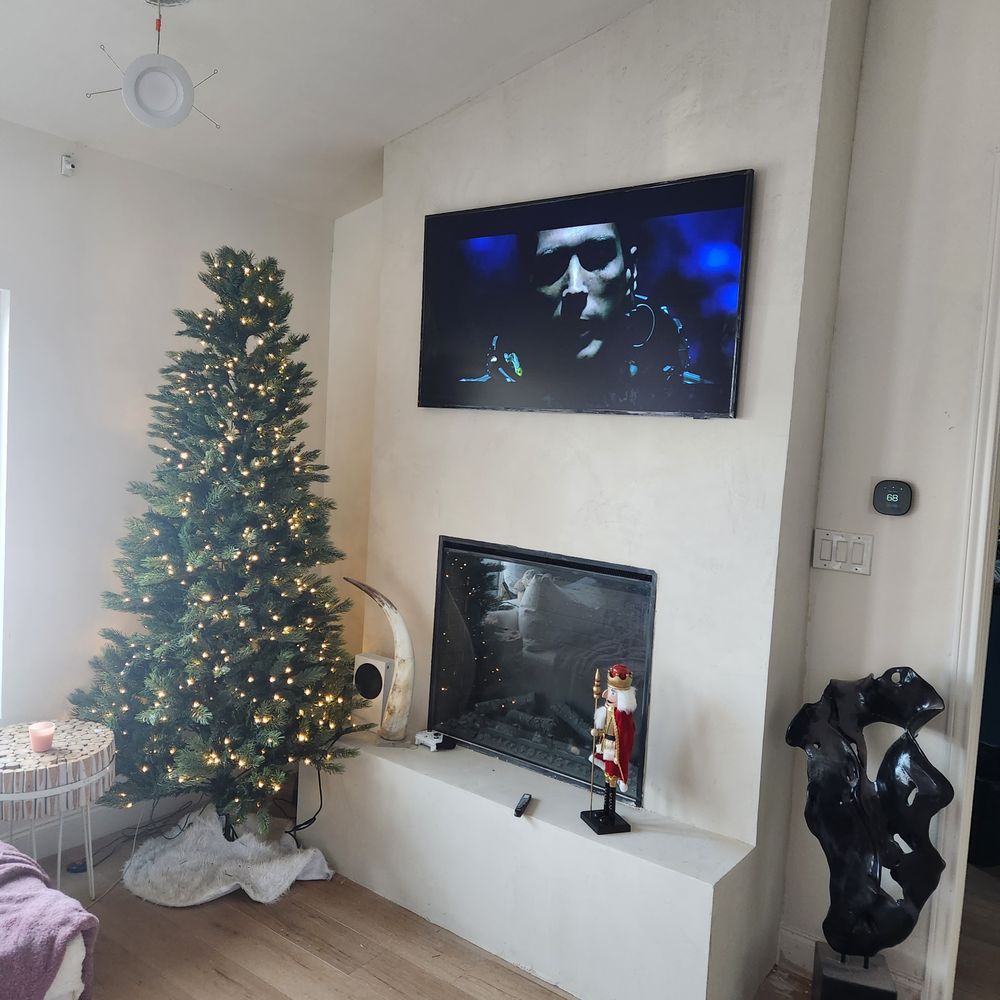 Living room with a Christmas tree, fireplace with TV, and decorative art.