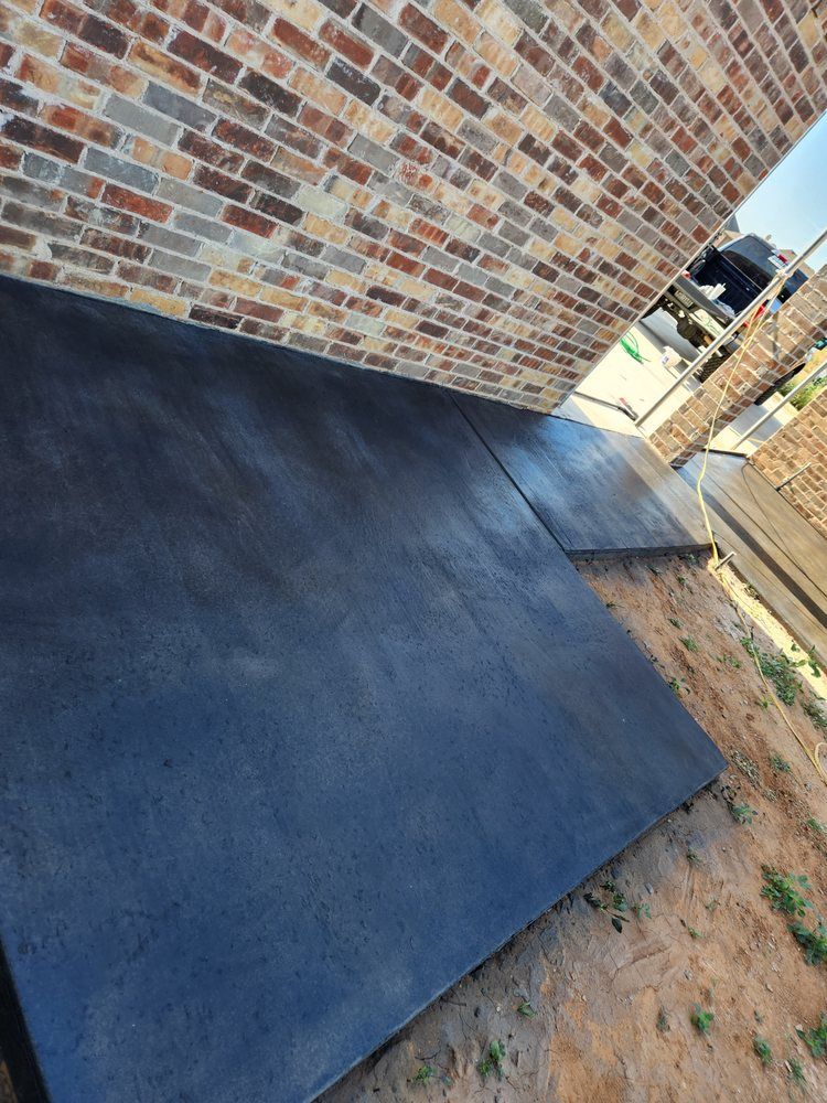 Dark gray concrete patio against a brick wall, outdoors in sunlight.