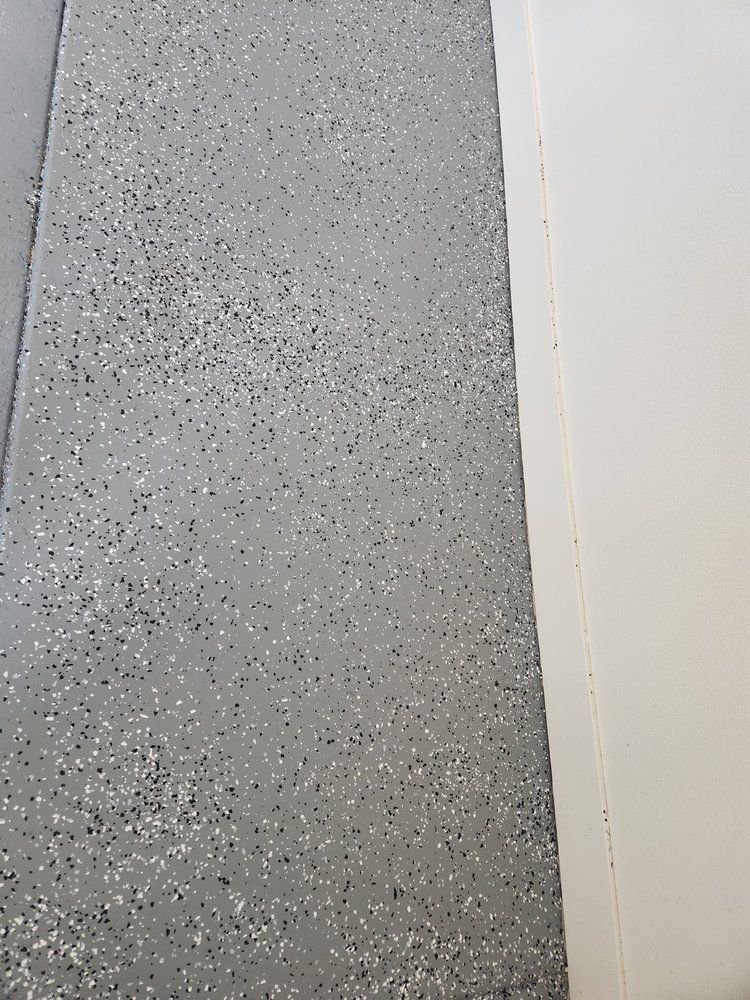 Gray speckled garage floor next to a white wall.