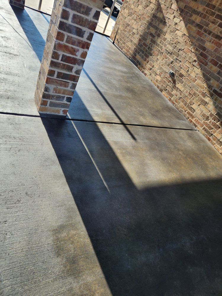 Brick pillar casting a long shadow on a dark concrete patio next to a brick wall.