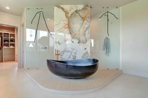 Modern bathroom with a black tub, a marble pillar, and a glass shower area.