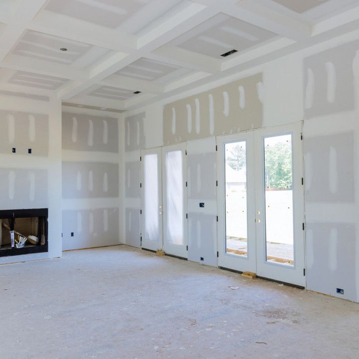 Interior under construction; drywall covers walls, ceiling. French doors lead outside, fireplace on left.