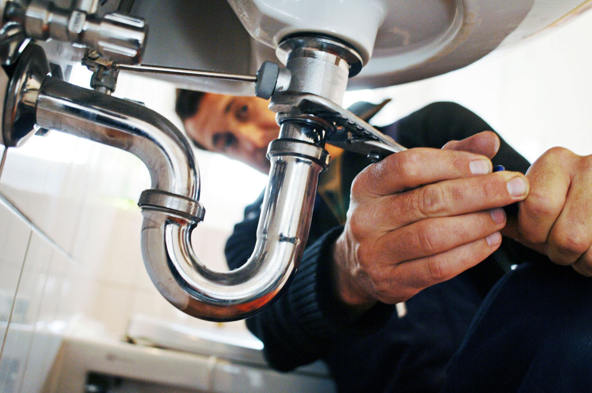 Close-up of a plumber repairing a sink with a tool in a bathroom.