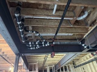 Exposed ceiling with black pipes and ducts in an unfinished industrial space