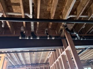 Exposed ceiling joists and black ductwork in an unfinished interior space