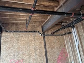 Interior of a construction site with exposed wood framing and black pipes on the ceiling
