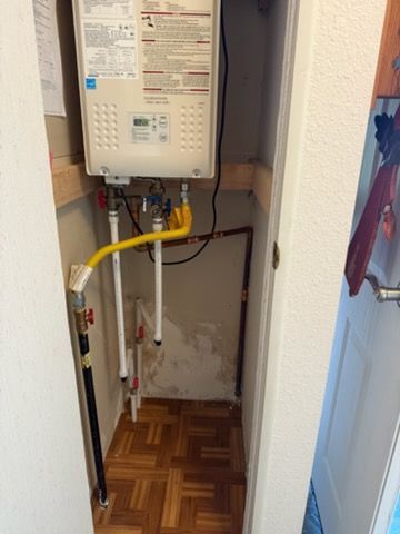 Indoor utility closet with a wall-mounted gas water heater, exposed pipes, and parquet flooring