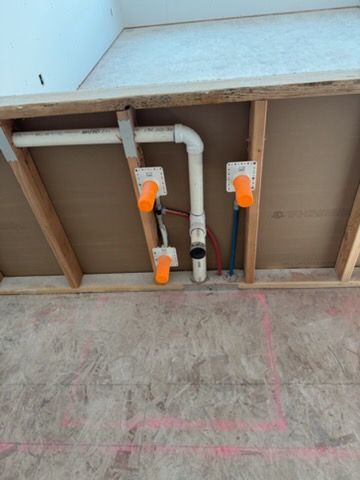Plumbing under a sink with white pipes, orange shutoff valves, and unfinished wood framing.