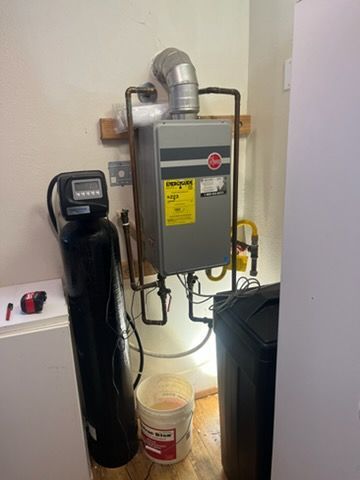 Water heater and filtration system in a utility room, with pipes, ducts, and a black tank beside them.