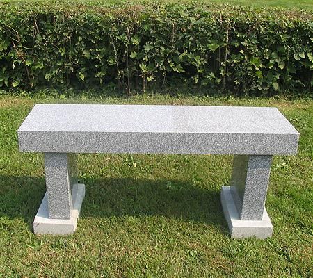 A stone bench is sitting in the grass in front of a hedge.