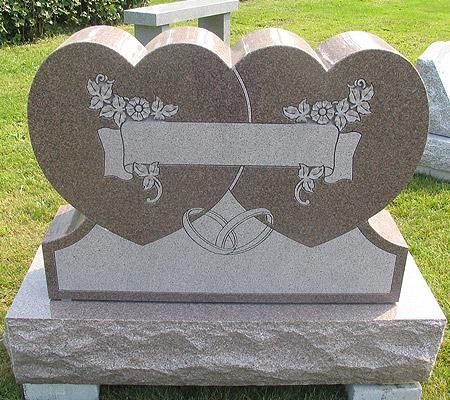 A gravestone in the shape of two hearts is sitting in the grass.