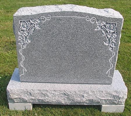 A gravestone with a floral design on it is sitting in the grass.