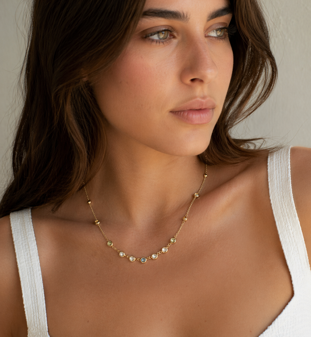 Portrait rapproché d'une femme portant un débardeur blanc et un collier en or, regardant sur le côté