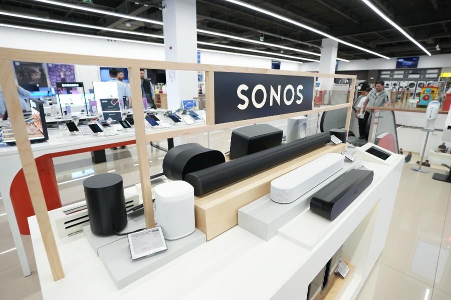 A sonos sign is above a display of speakers in a store.