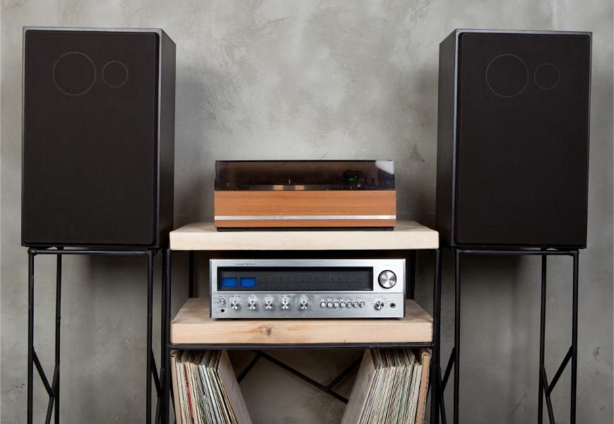 A record player is sitting on top of a wooden shelf next to two speakers.
