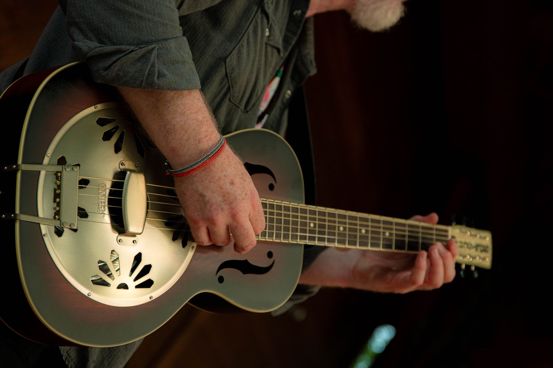 Man playing a resonator guitar, close-up. Silver body, brown trim.