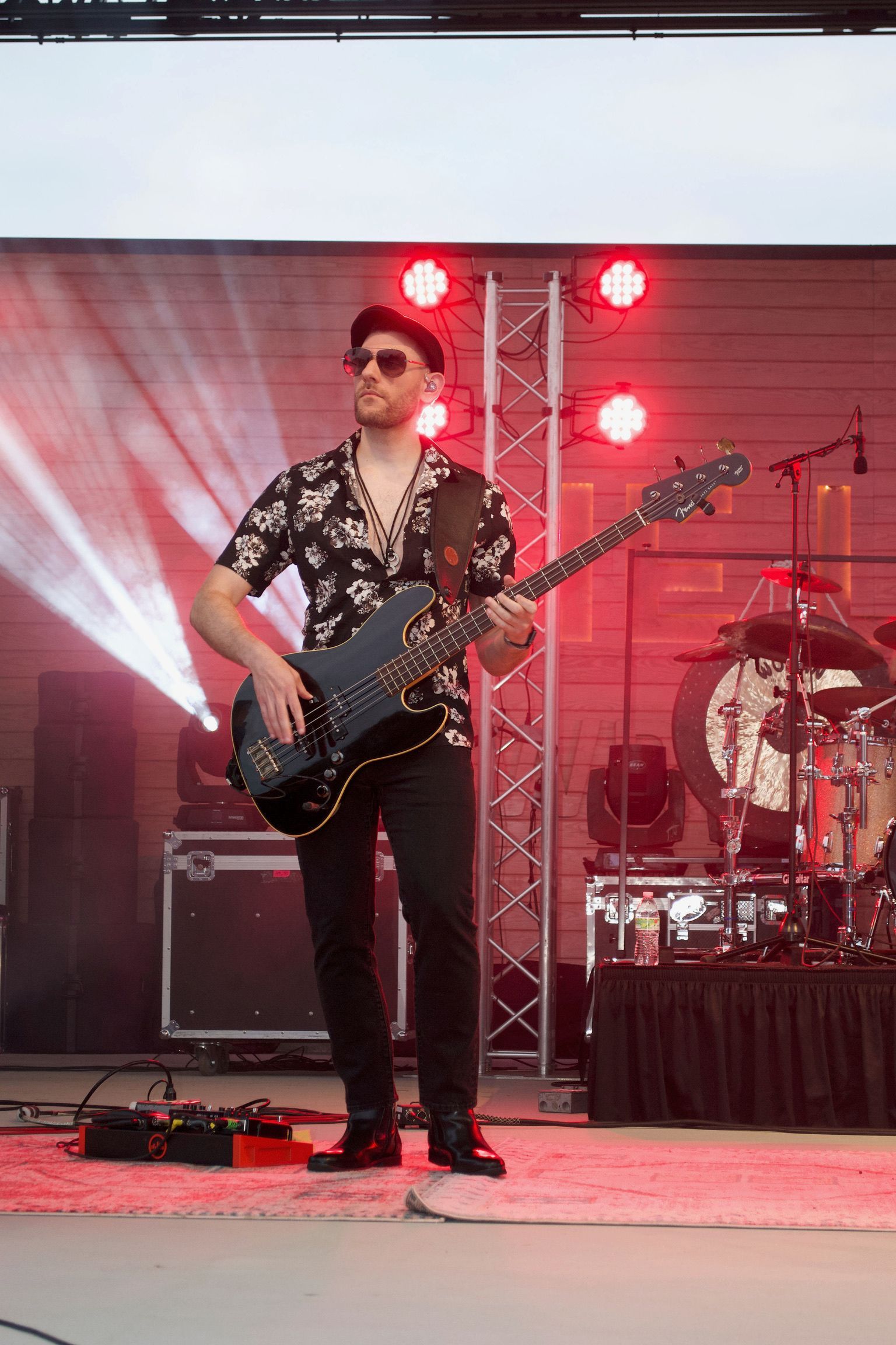 Bass player in a floral shirt and black pants on stage with red lighting.