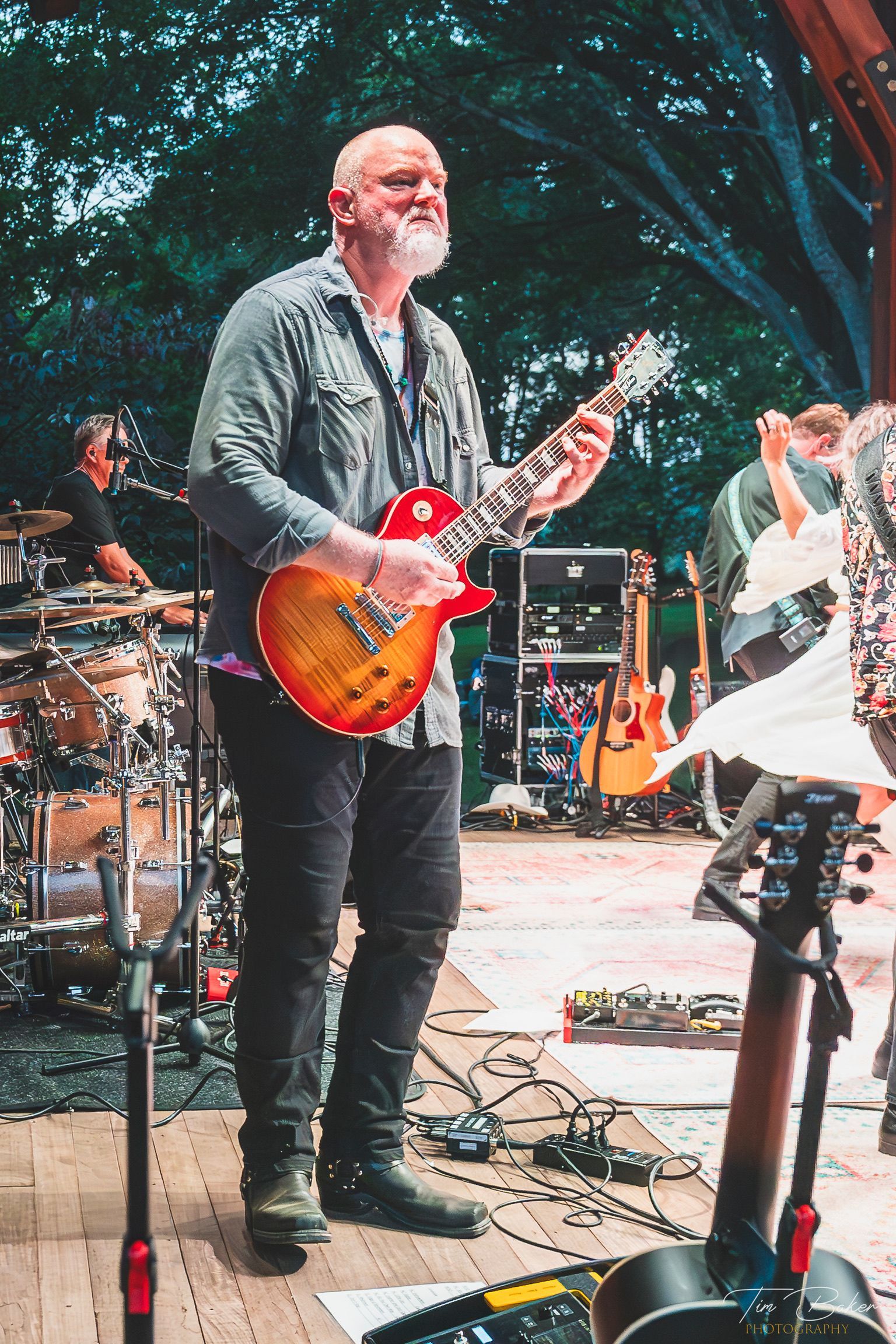 Man playing a red electric guitar onstage at an outdoor concert.