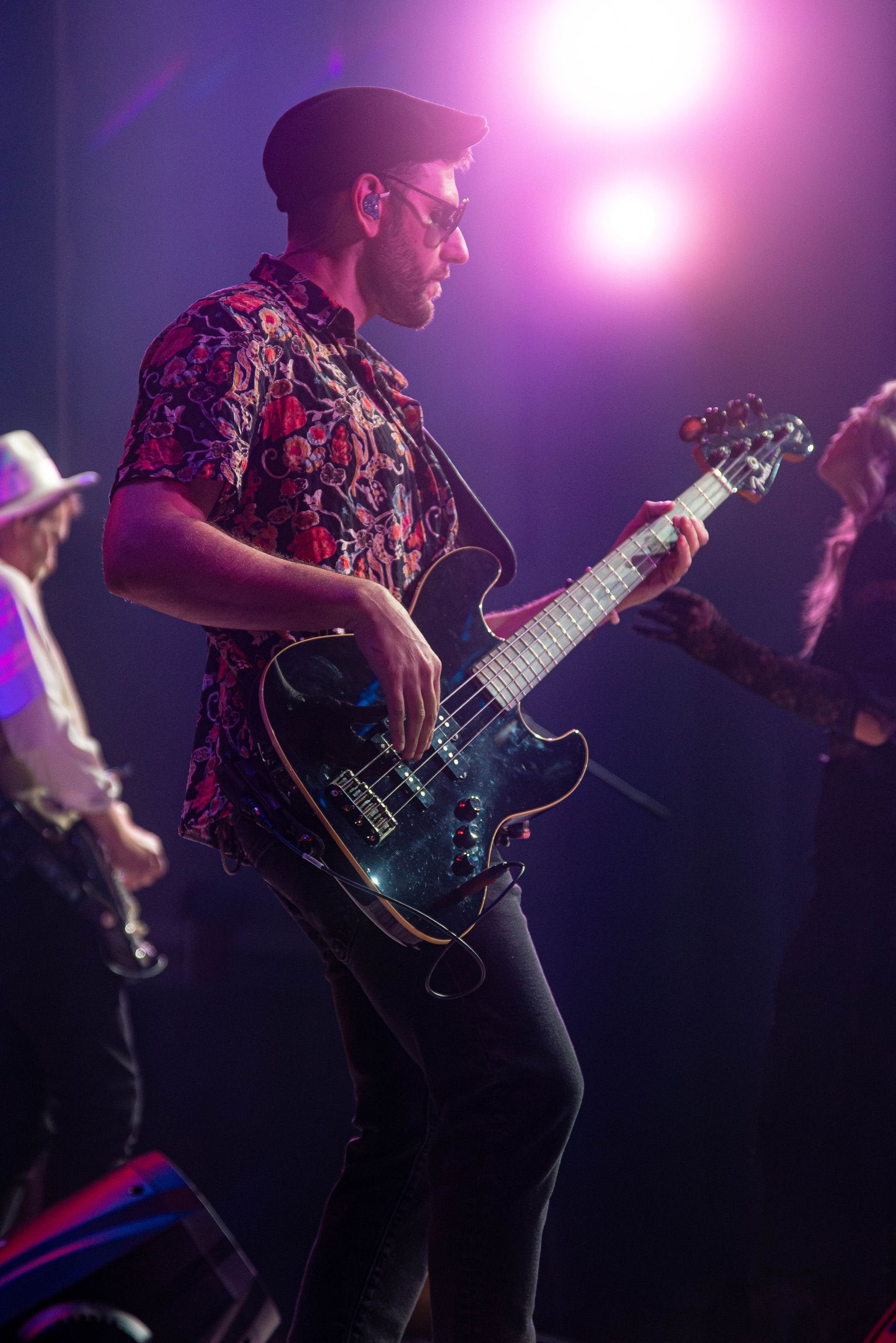 Bass guitarist onstage in a colorful shirt and black pants, playing under stage lights.