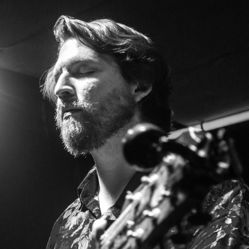 Man singing into a microphone, mouth open, smiling. Black and white close-up.