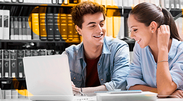 Dos estudiantes sonriendo, mirando una computadora portátil en una biblioteca.