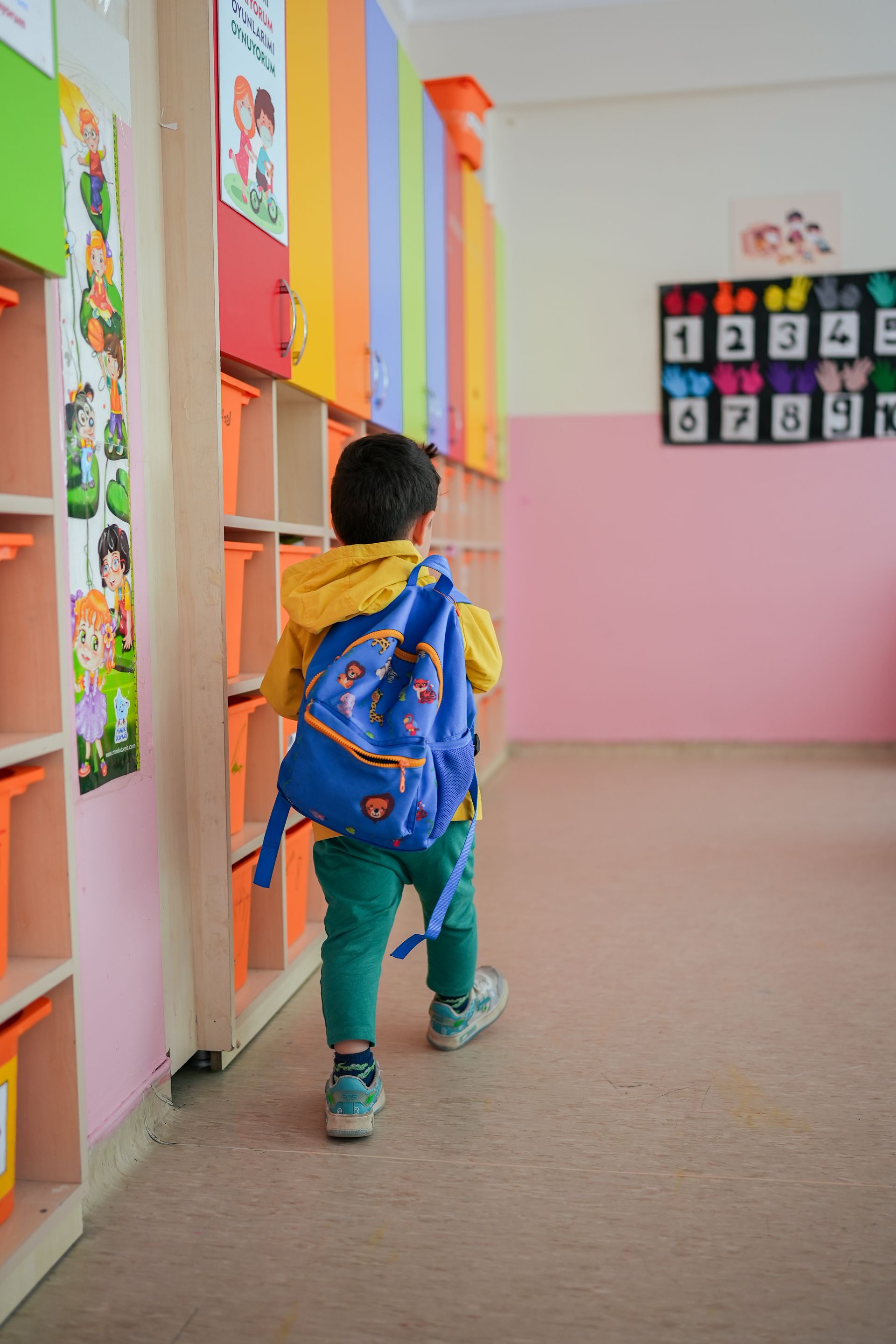 Un niño con una mochila azul camina por un colorido pasillo escolar pasando por los casilleros.