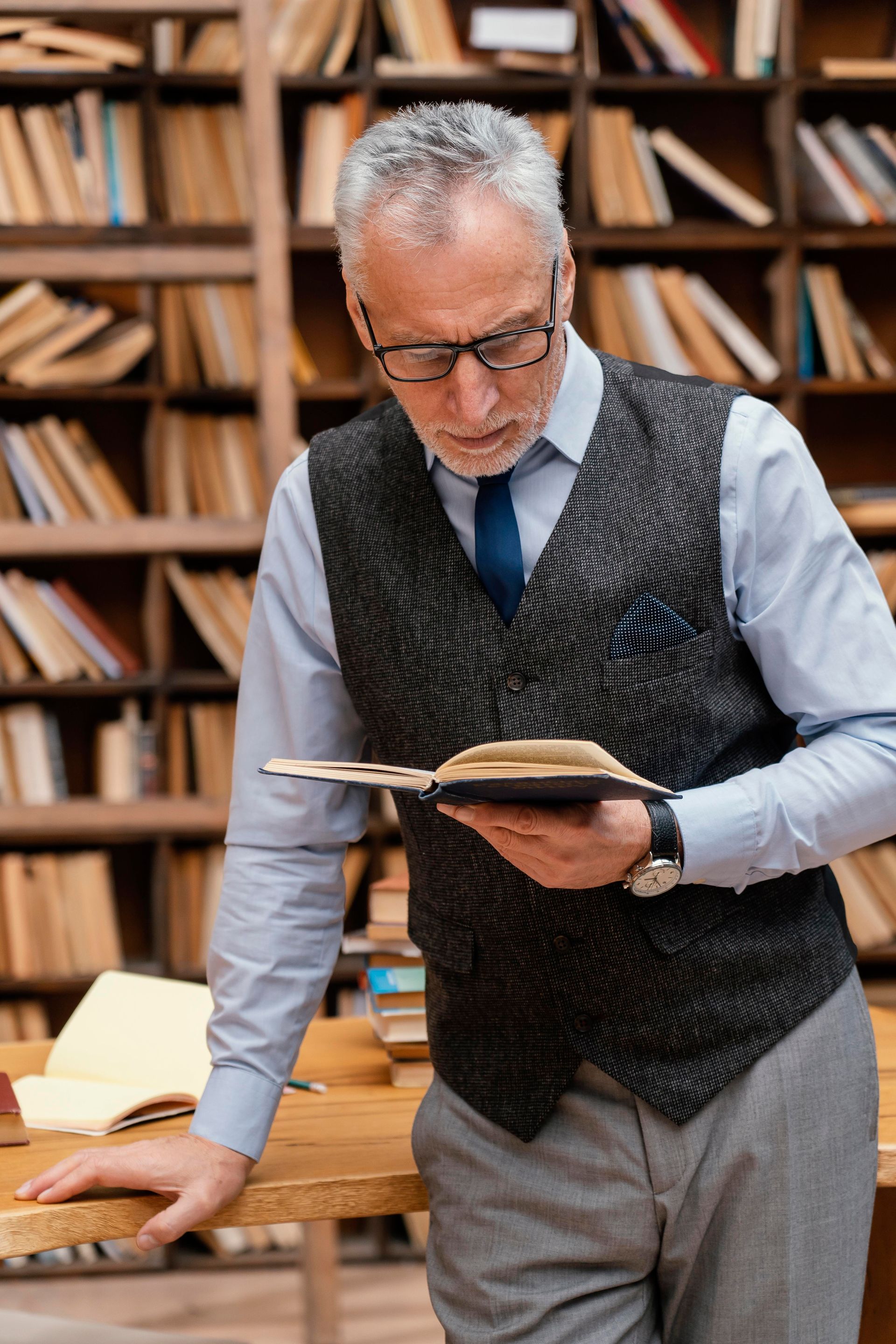Hombre con gafas leyendo un libro en la biblioteca.