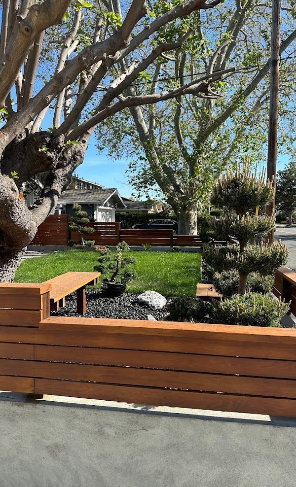 A wooden fence surrounds a lush green yard with trees and bushes.