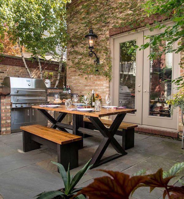 A patio with a table and benches and a grill