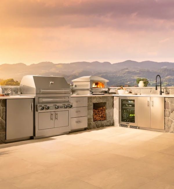 A kitchen with a grill , sink , refrigerator and mountains in the background.