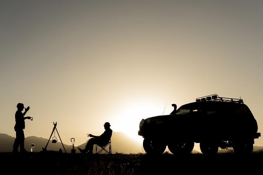 A Silhouette Of Two Men Standing Next To A Car At Sunset — TJM Dubbo In Dubbo, NSW