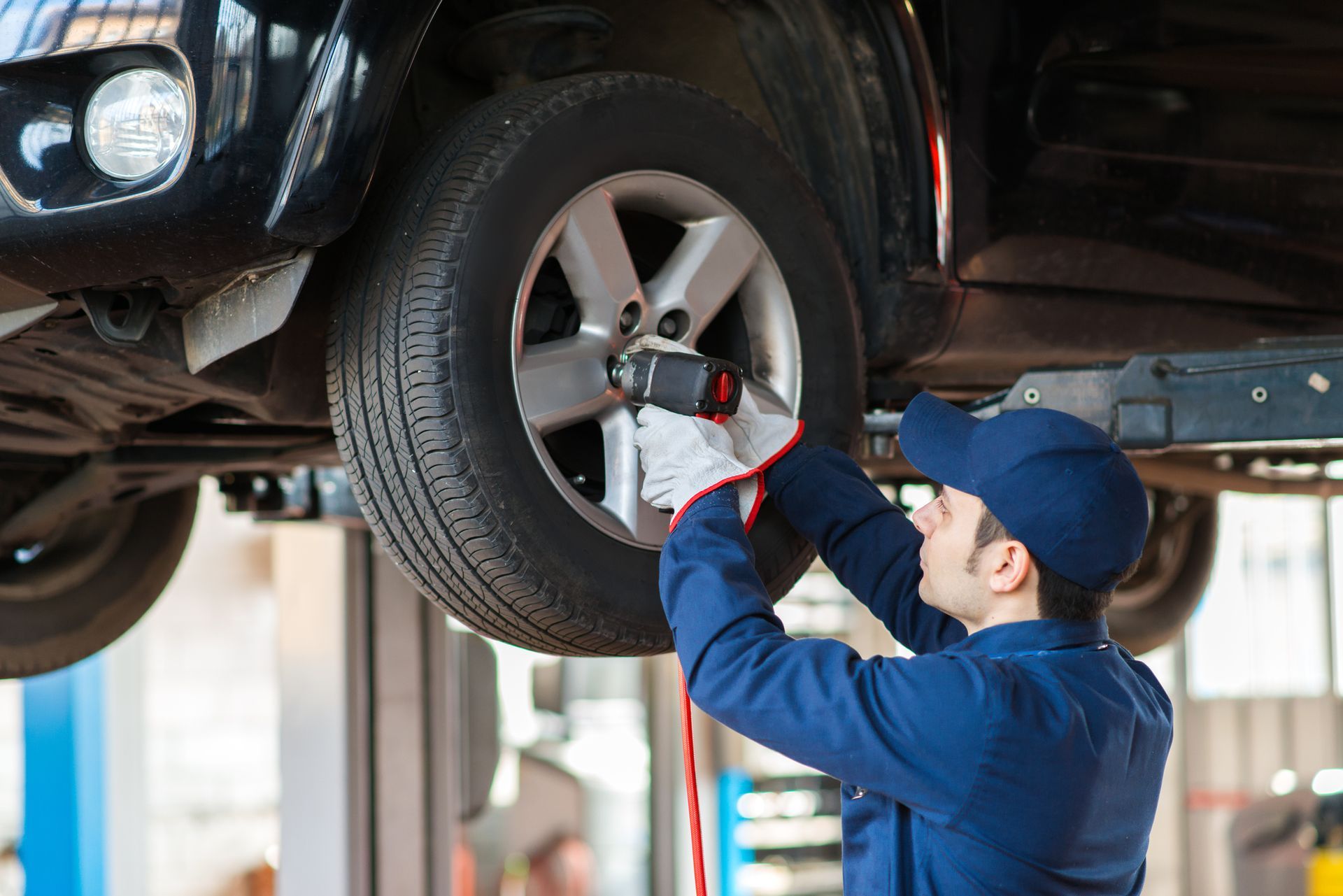 Mechanic wearing a blue uniform, performing tyre placement in a car, at an auto shop.