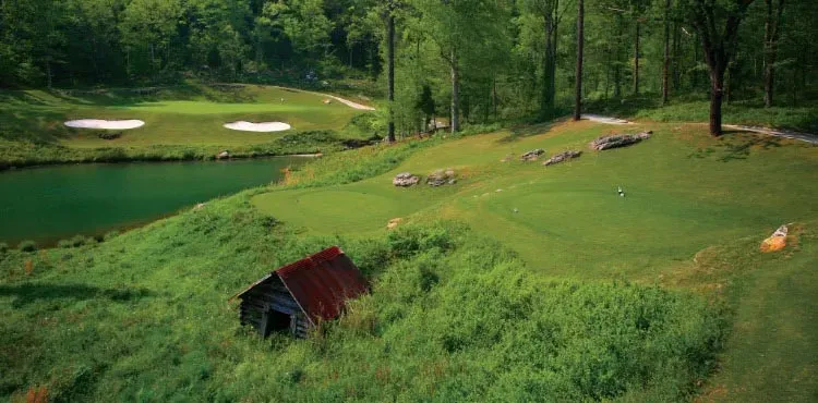 An aerial view of a golf course with a small house in the middle of it.