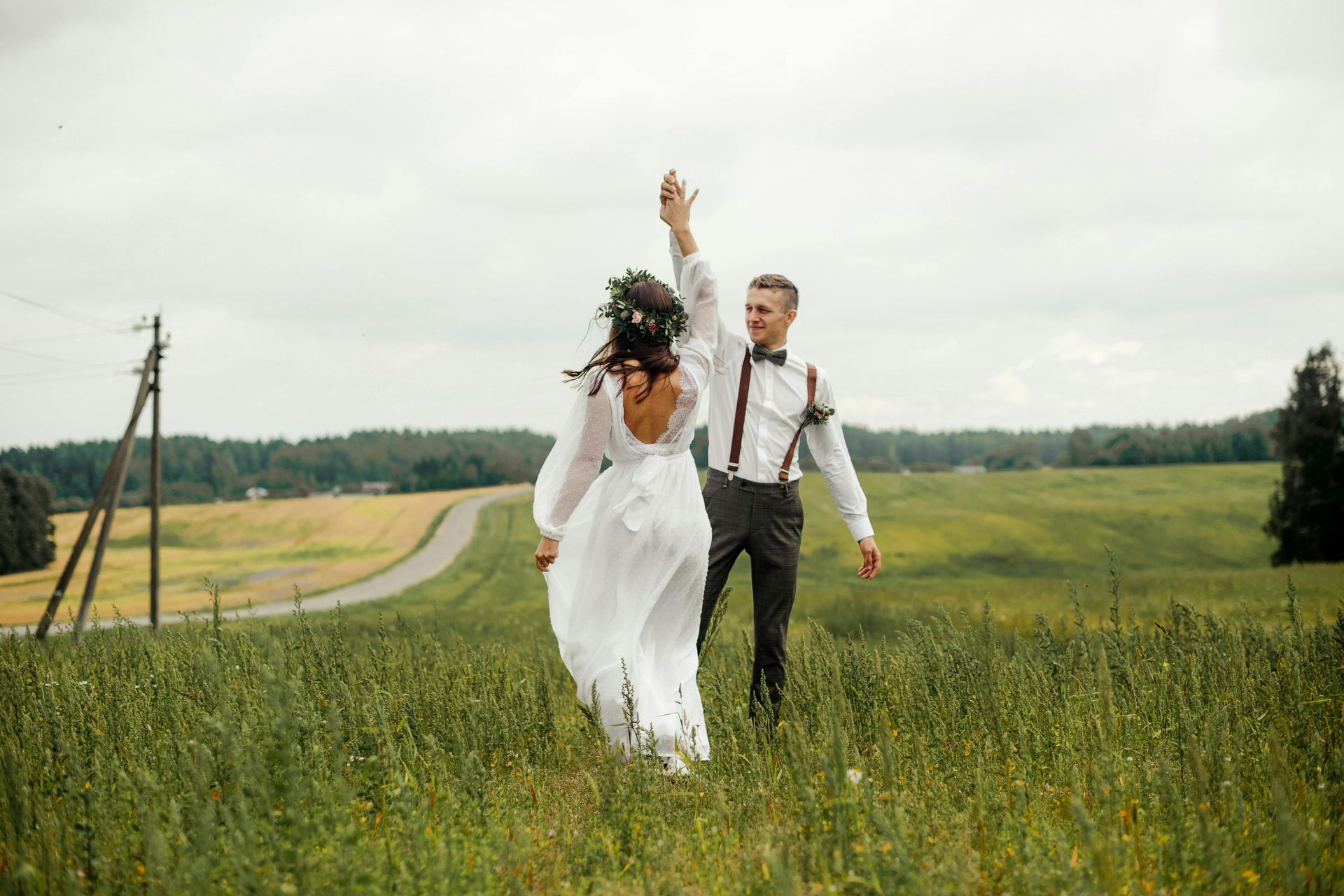 A bride and groom are running through a grassy field.