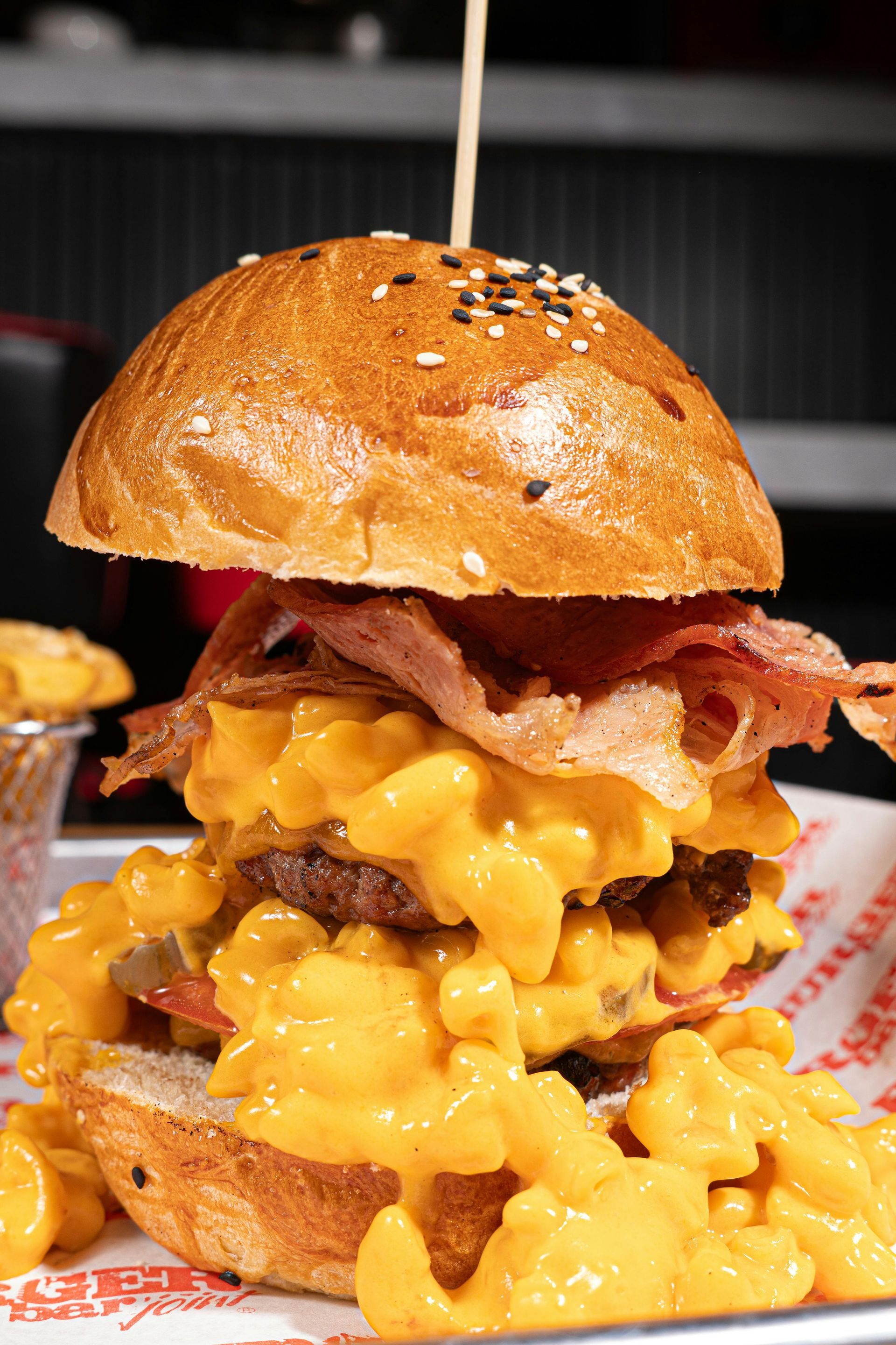 A close up of a hamburger with cheese , bacon and macaroni and cheese on a plate.