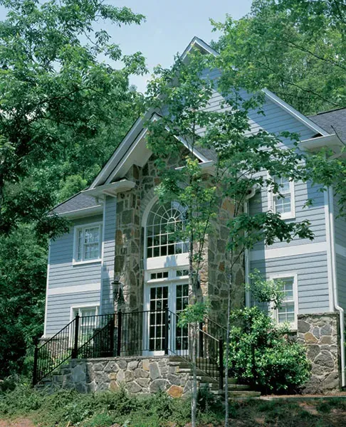 A large house with a stone facade is surrounded by trees
