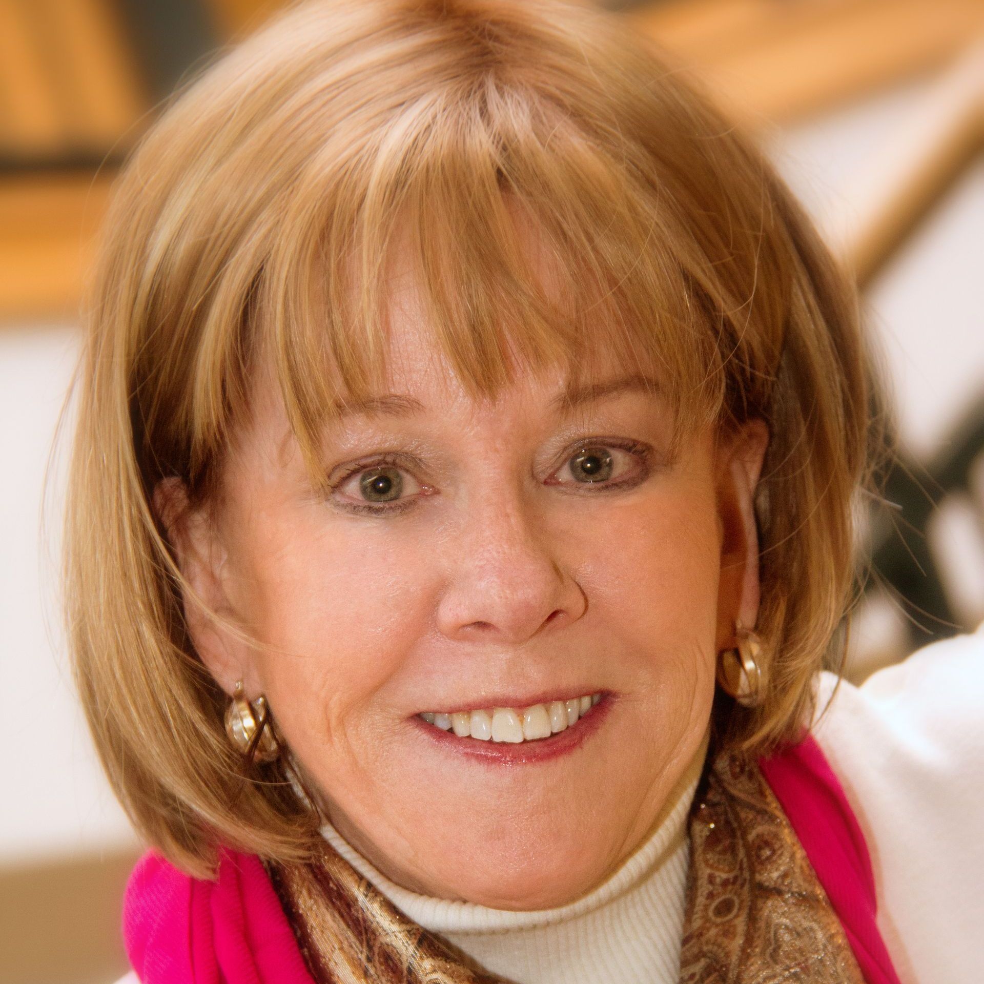 A woman wearing a pink scarf and earrings is smiling for the camera.