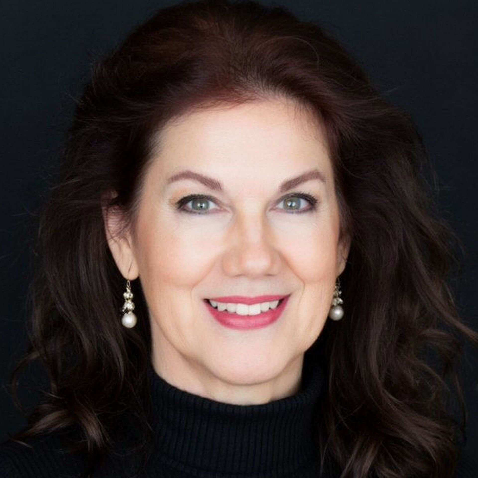 A woman with long dark hair is wearing a blue shirt and earrings.