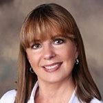 A woman with long brown hair and bangs is smiling for the camera.