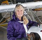 A woman in a purple jacket is sitting next to a small plane.