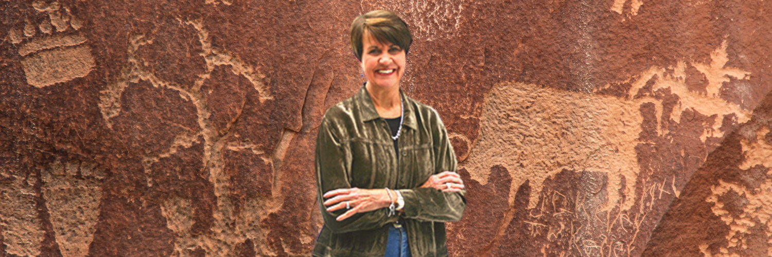 A woman is standing in front of a wall with petroglyphs on it