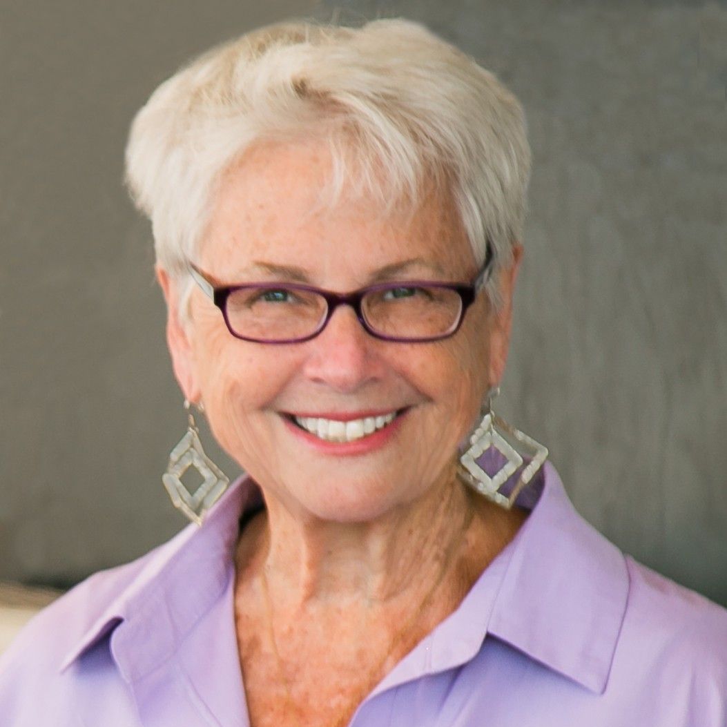 A woman wearing glasses and a purple sweater is smiling for the camera.